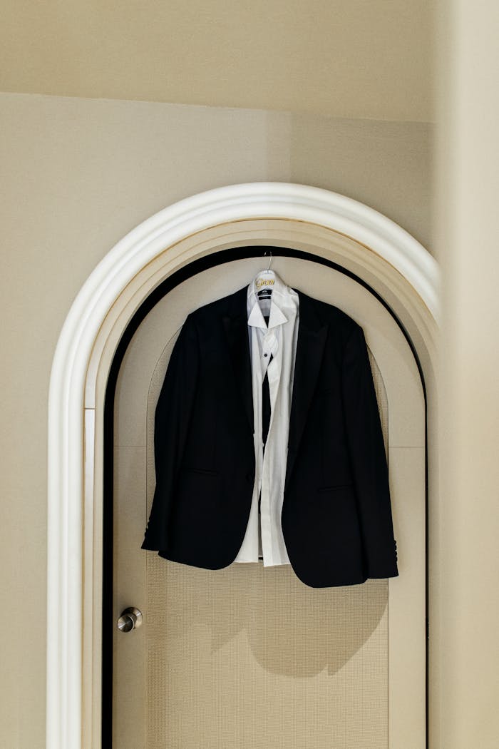 home-hero Classic black suit and white shirt hanging on an arched door, showcasing elegance and sophistication.