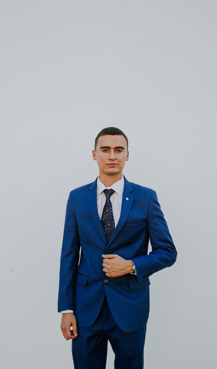 services-05 A confident man in a stylish blue suit poses against a plain background, exuding elegance and professionalism.